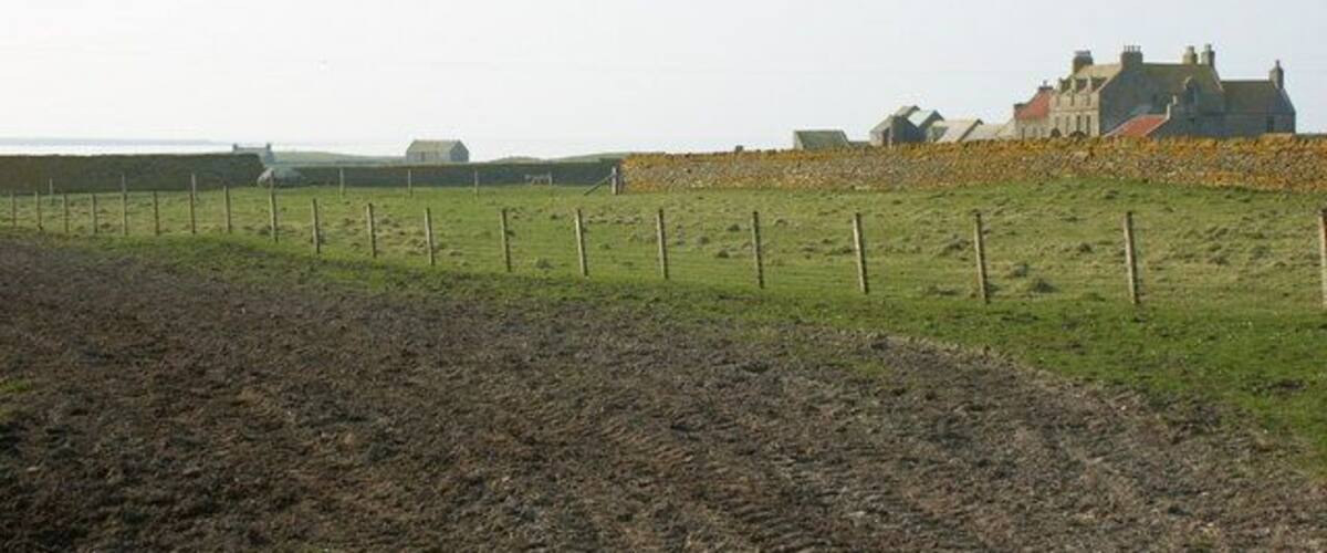 A plowed field, a fence, and a building in the background.