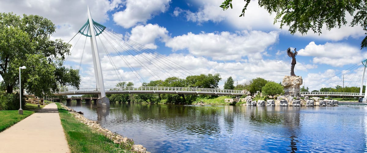 A river with a bridge, a statue, and a park with trees and a walkway.