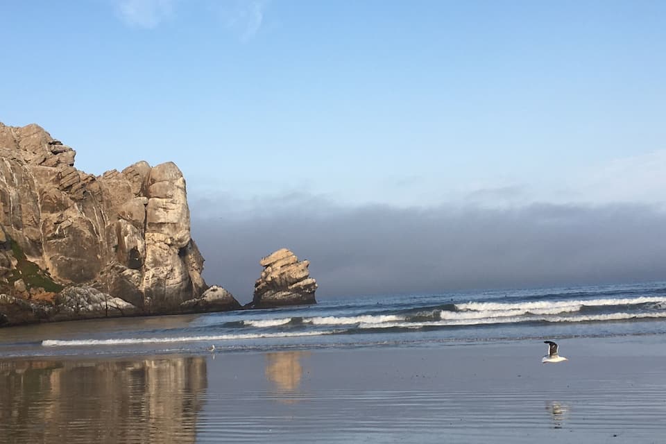 A beach with rocky cliffs and calm waves.