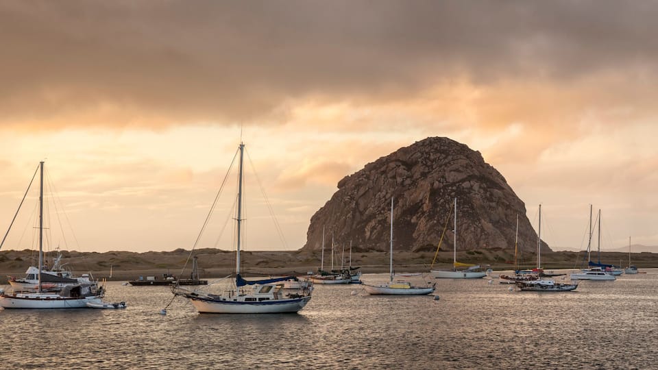 A rocky formation surrounded by boats on calm water.