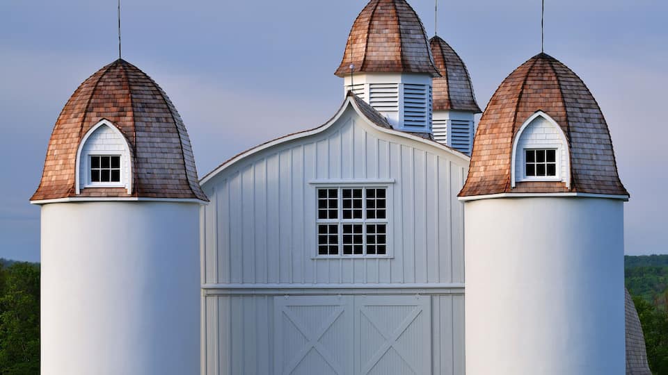 A white barn with three conical roofs and a central window.