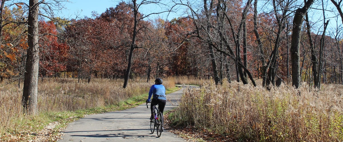Man riding a bicycle in fall on a sunny day at Miami Woods on the North Branch Trail in Morton Grove, Illinois