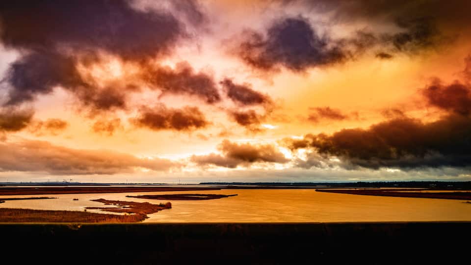 A sunset over a coastal landscape with a river and marshy areas.