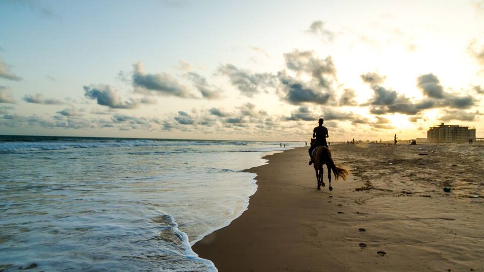 A beach with a horse and rider walking along the shore.