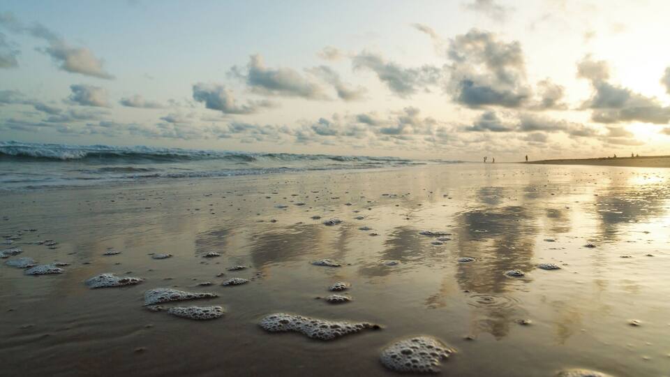 A beach with foamy waves and a cloudy sky.