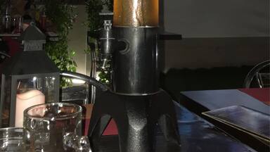 A lava lamp on a table with a TV screen in the background displaying a person.