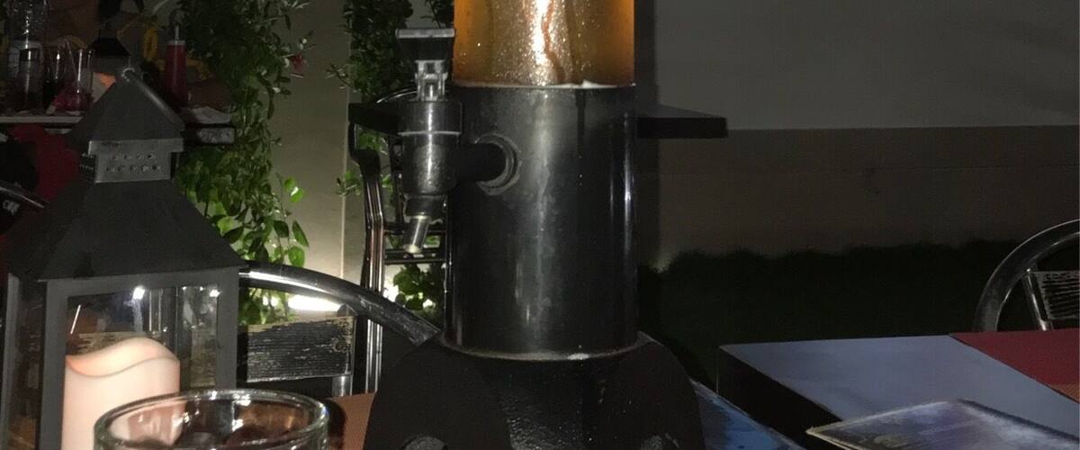 A lava lamp on a table with a TV screen in the background displaying a person.