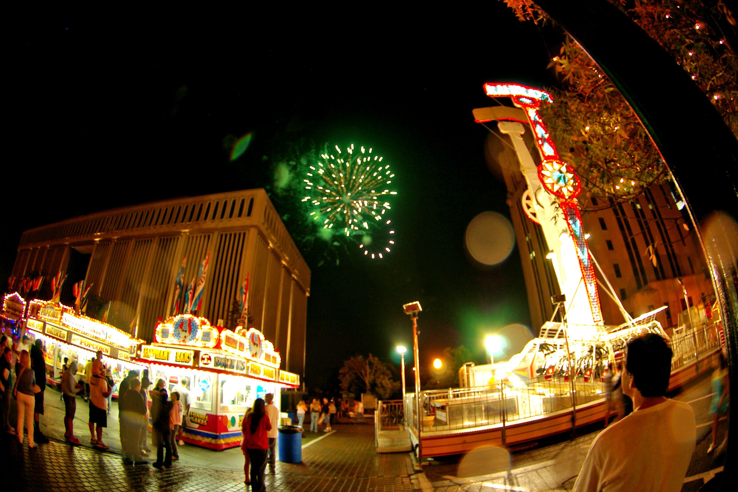 A nighttime amusement park with a Ferris wheel, carousel, and fireworks display.