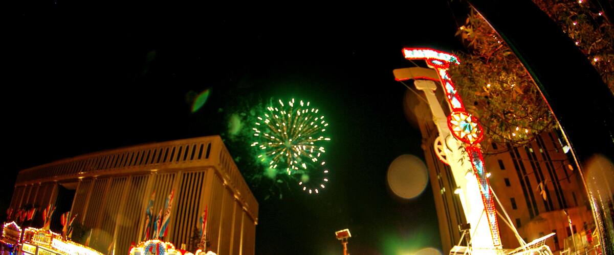 A nighttime amusement park with a Ferris wheel, carousel, and fireworks display.