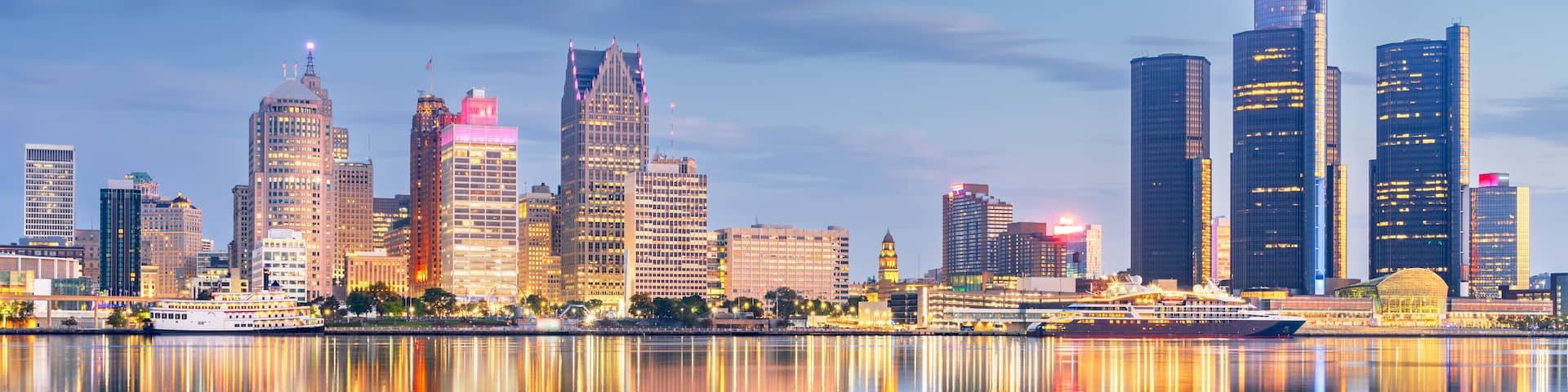 A city skyline with illuminated buildings reflected in calm water.