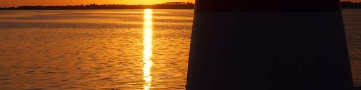 Un phare au coucher du soleil, avec le soleil qui se reflète sur l’eau.