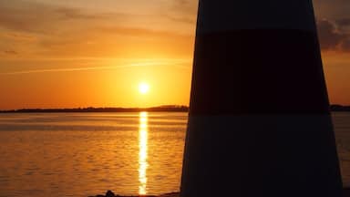 Um farol ao pôr do sol, com o sol refletindo na água.