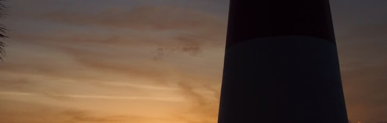 A lighthouse at sunset with the sun reflecting on the water.