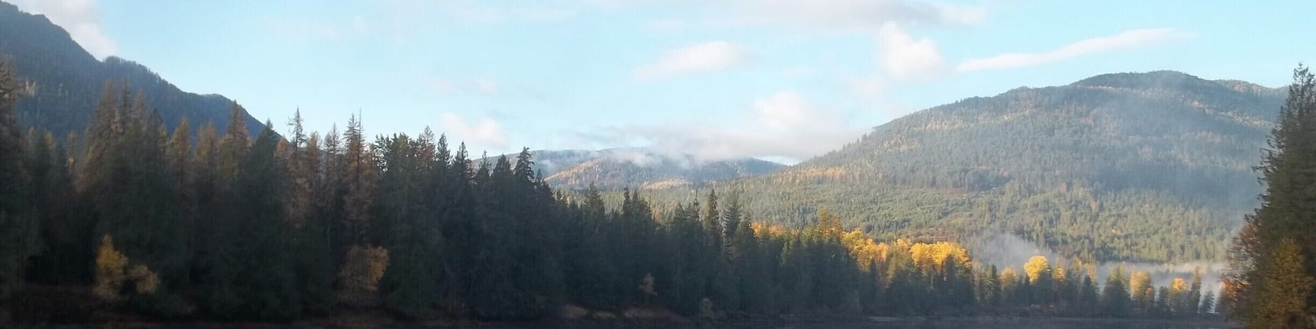 A calm lake surrounded by forested hills, with clear reflections of the sky and trees.