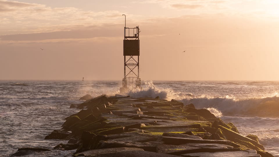 Breakwater Rocks with Crashing Waves at the Ocean with Golden Sunrise Light