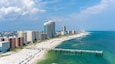 A coastal cityscape with a long sandy beach, a pier extending into the ocean, and high-rise buildings.