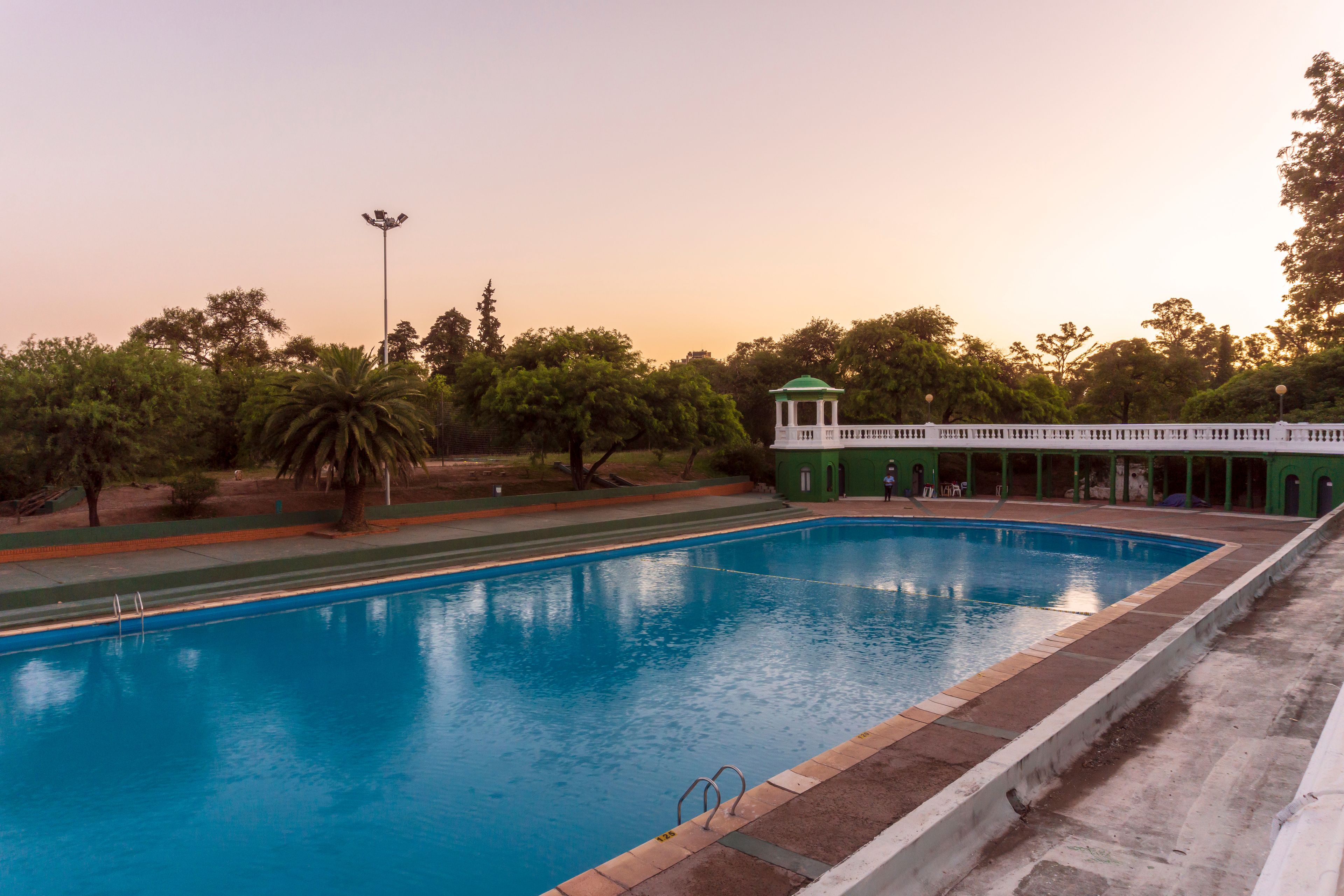 A swimming pool with a green-roofed pavilion and trees in the background.