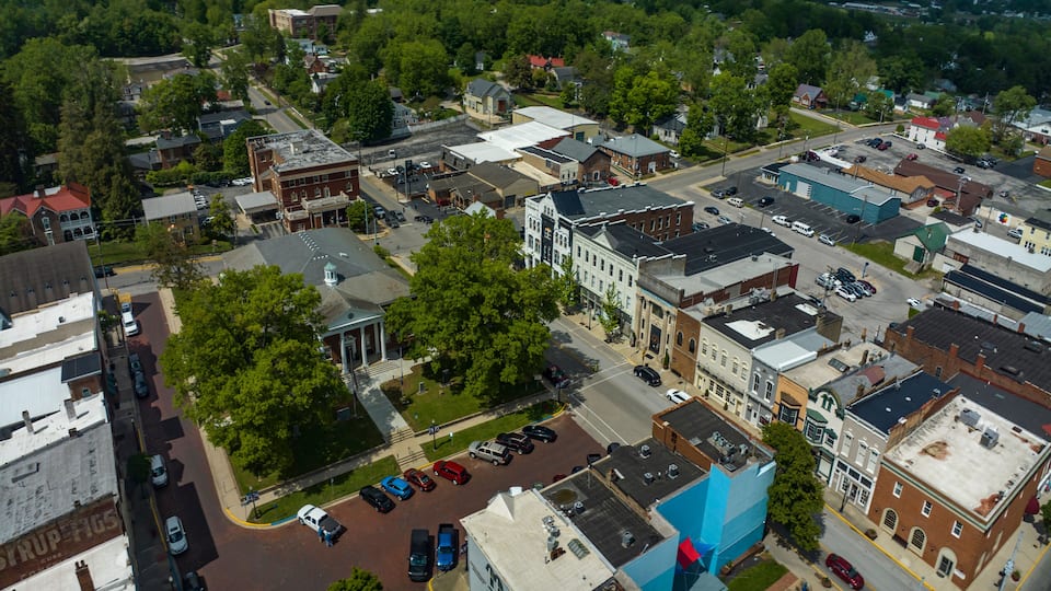 An aerial view of a town with historic buildings, a central green area, and a parking lot.
