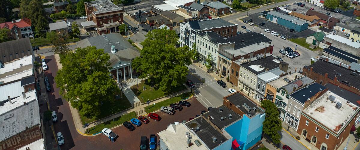 An aerial view of a town with historic buildings, a central green area, and a parking lot.