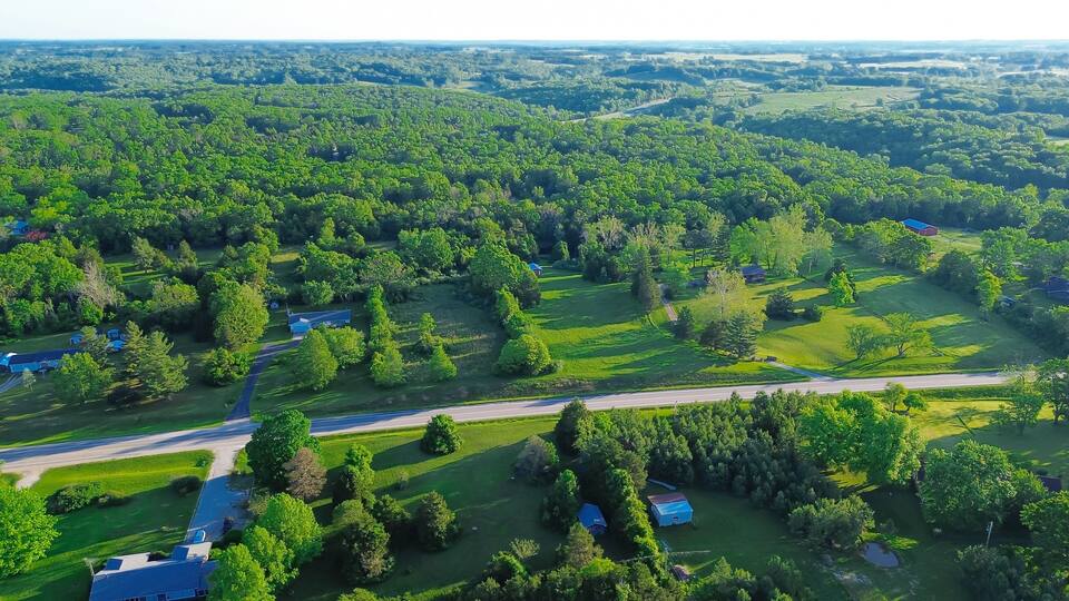 Country road US-60 BUS in rural Mountain Grove Missouri through lush greenery trees acreage, meadows and farm houses with ponds in agricultural area, peaceful countryside in Midwest, aerial view