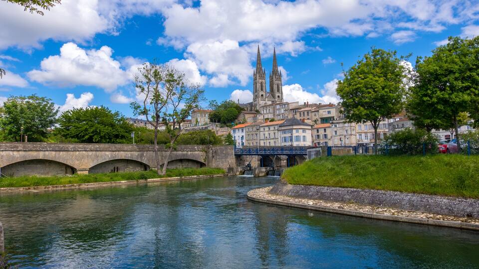 A river with a bridge, a cathedral, and surrounding greenery.