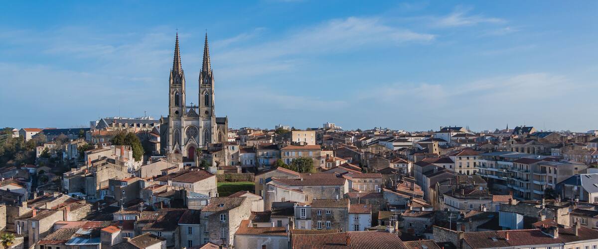 A historic cityscape with a prominent cathedral featuring twin spires and a large rose window.
