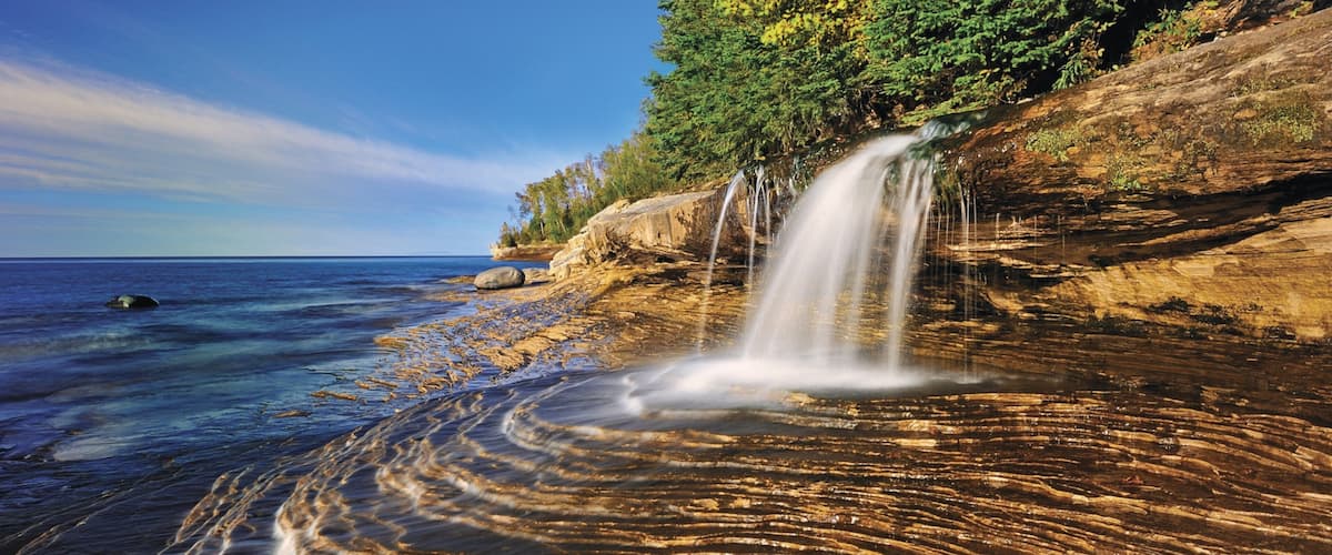 A coastal landscape with a waterfall, clear water, and rocky terrain.