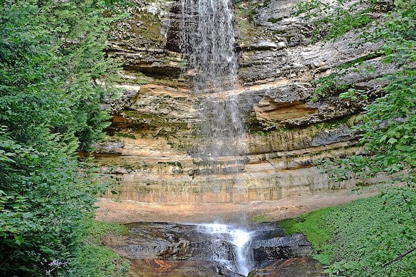 A waterfall cascading down a rocky cliff surrounded by lush greenery.