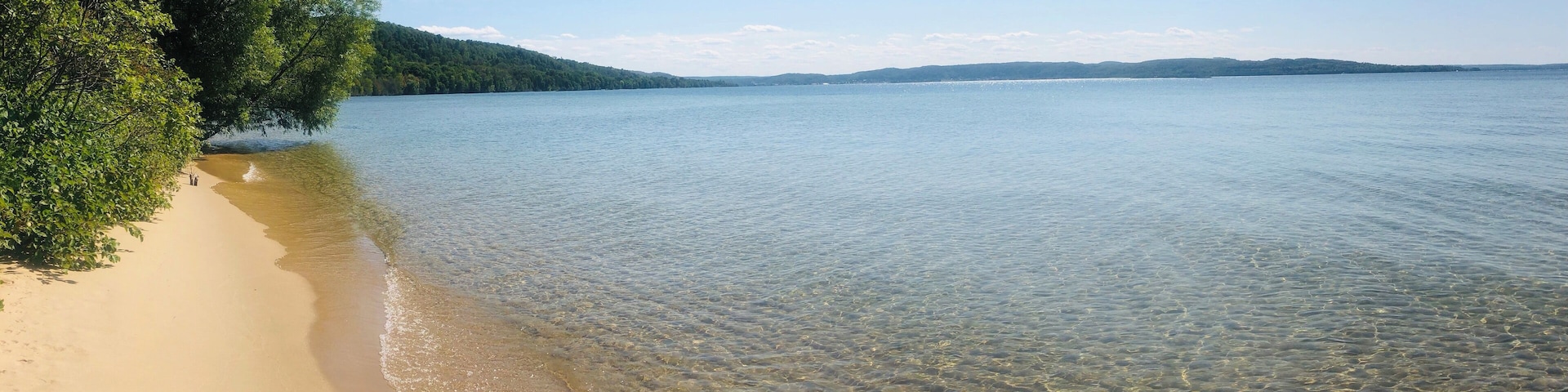 Ein klarer See mit Sandstrand und üppiger Vegetation am Ufer.