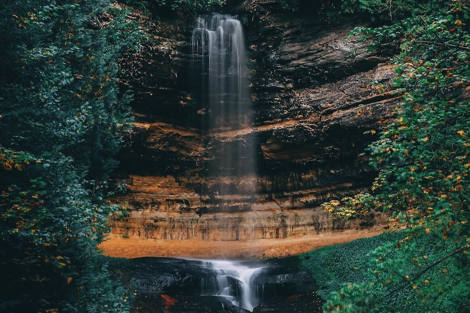 Una cascada se precipita por un risco rocoso rodeado de un bosque denso.