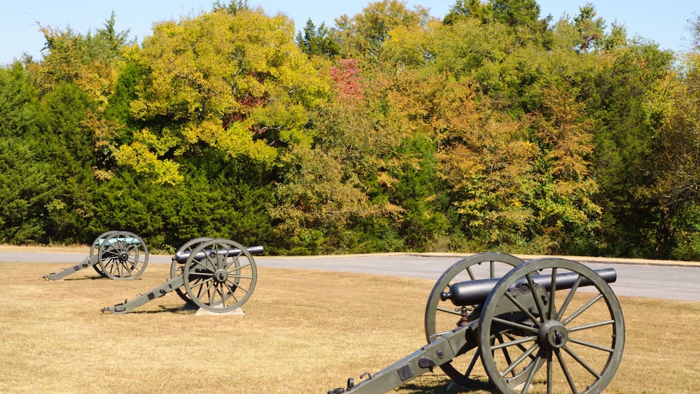 Three cannons in a field with autumn-colored trees in the background.