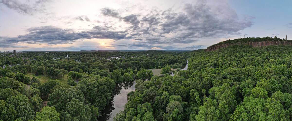 Aerial view of lush forest, river, cliff, and sky at East Rock Park, New Haven, Connecticut, United States.