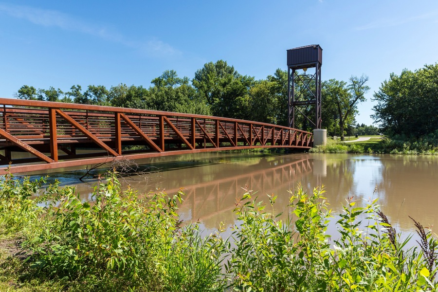 Un puente metálico sobre un río tranquilo con una torre de vigilancia al fondo.