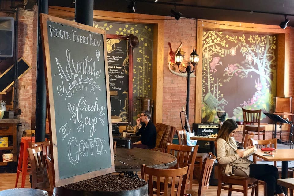 A cozy cafe with wooden furniture, a chalkboard sign, and a mural on the wall.