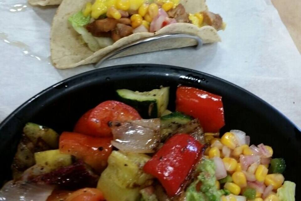 Three tacos with corn and lettuce, and a bowl of mixed vegetables and corn salad.