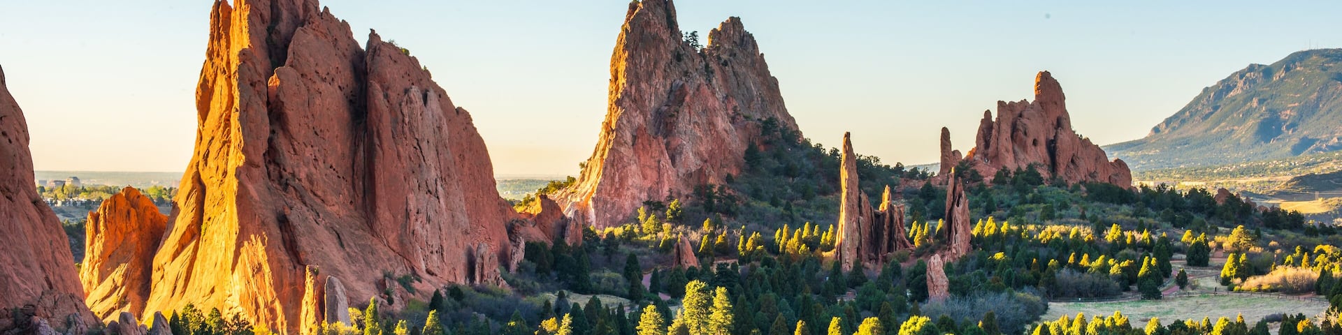 A landscape with prominent red rock formations and dense green trees.