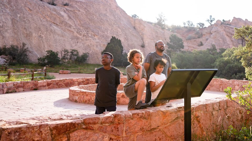 A group of people sitting on a stone bench with a large rock formation in the background.