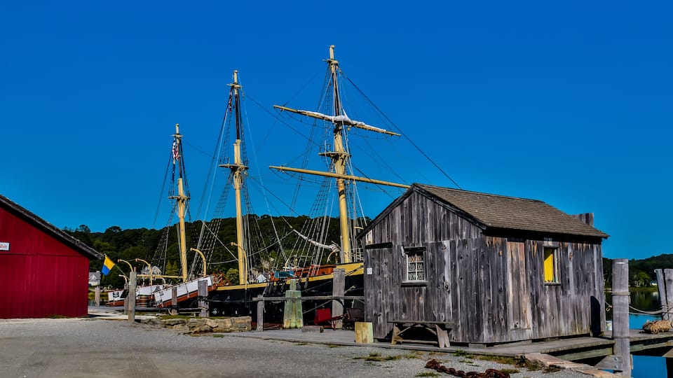 A historic ship docked at a pier with a wooden building nearby.
