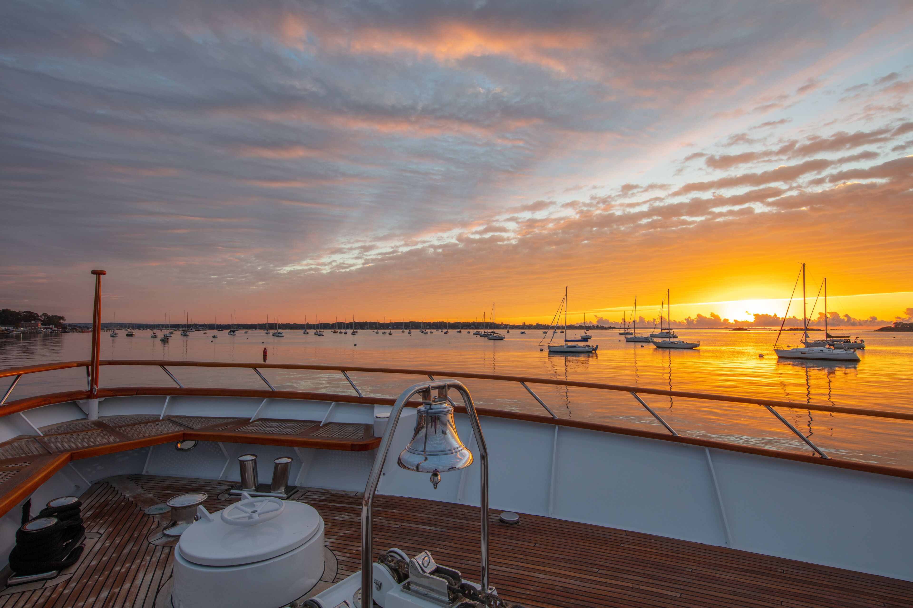 A sunset view from a boat deck with multiple sailboats anchored in the water.