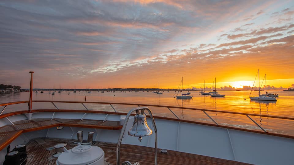 A sunset view from a boat deck with multiple sailboats anchored in the water.