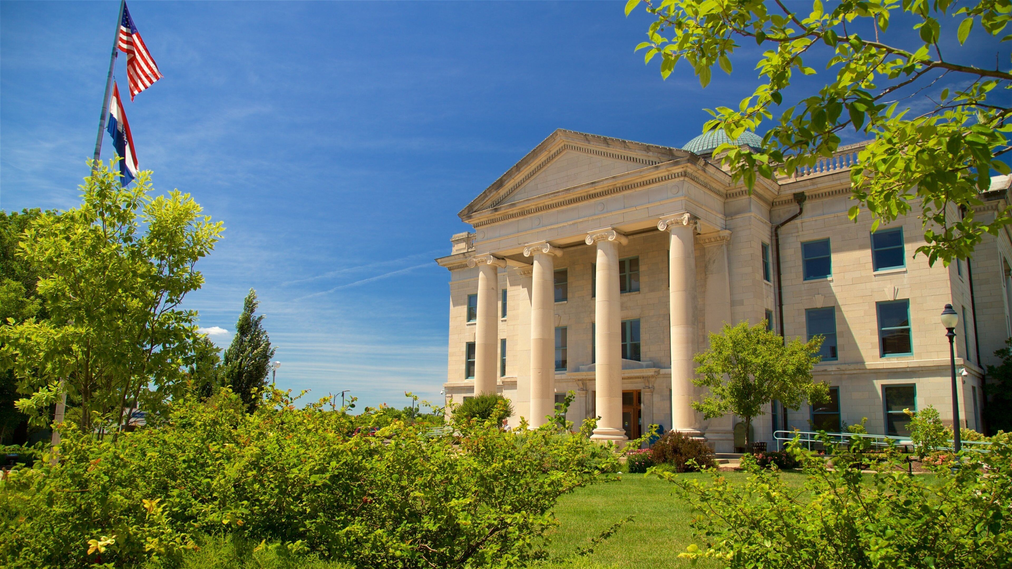 A neoclassical building with columns, surrounded by lush greenery and an American flag.