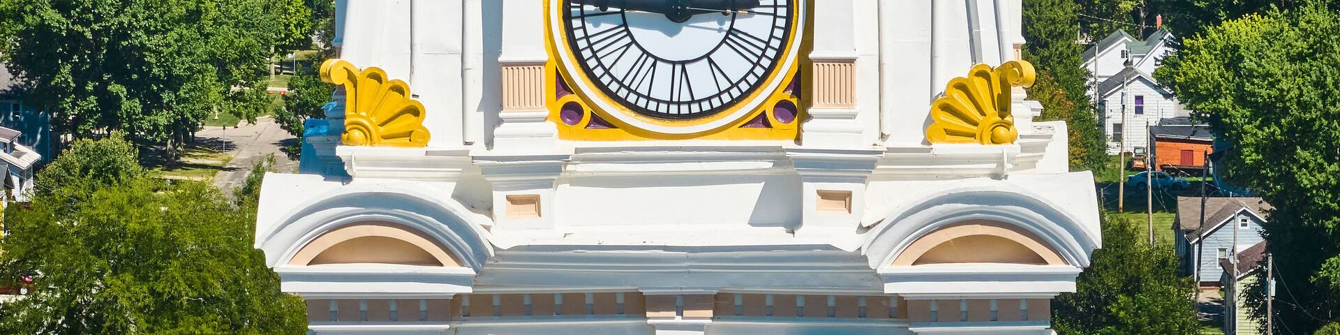 A large clock tower with a white and yellow facade, surrounded by trees.