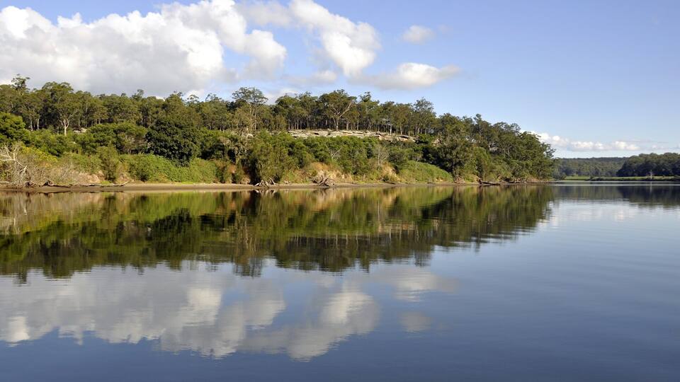 A calm lake with a reflection of trees and clouds.