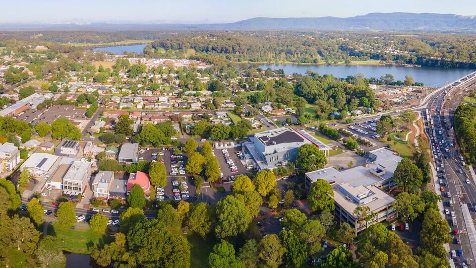 An aerial view of a town with a bridge, a lake, and surrounding greenery.