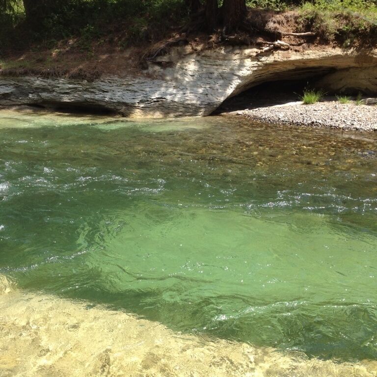 A clear river with a rocky bank and a small cave-like formation.