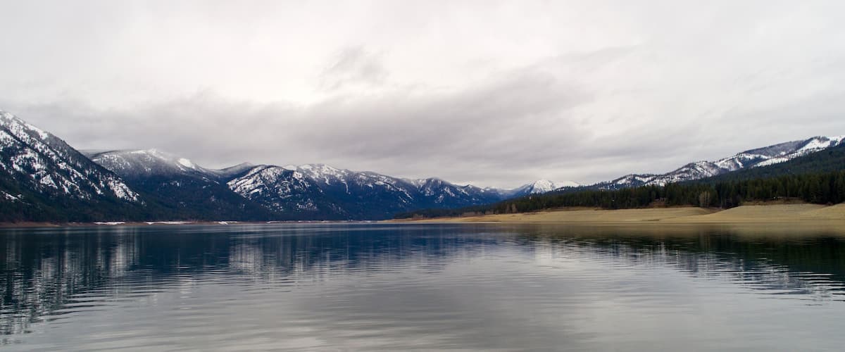 A calm lake with snow-capped mountains in the background.