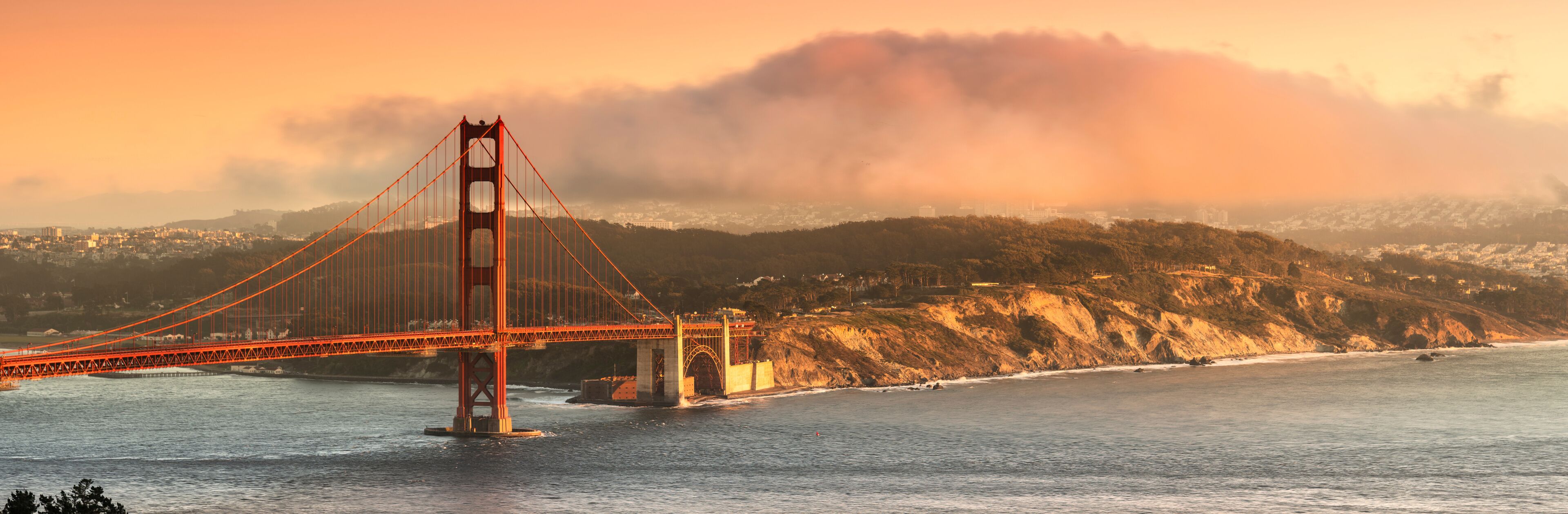 The Golden Gate Bridge with a backdrop of fog and hills.