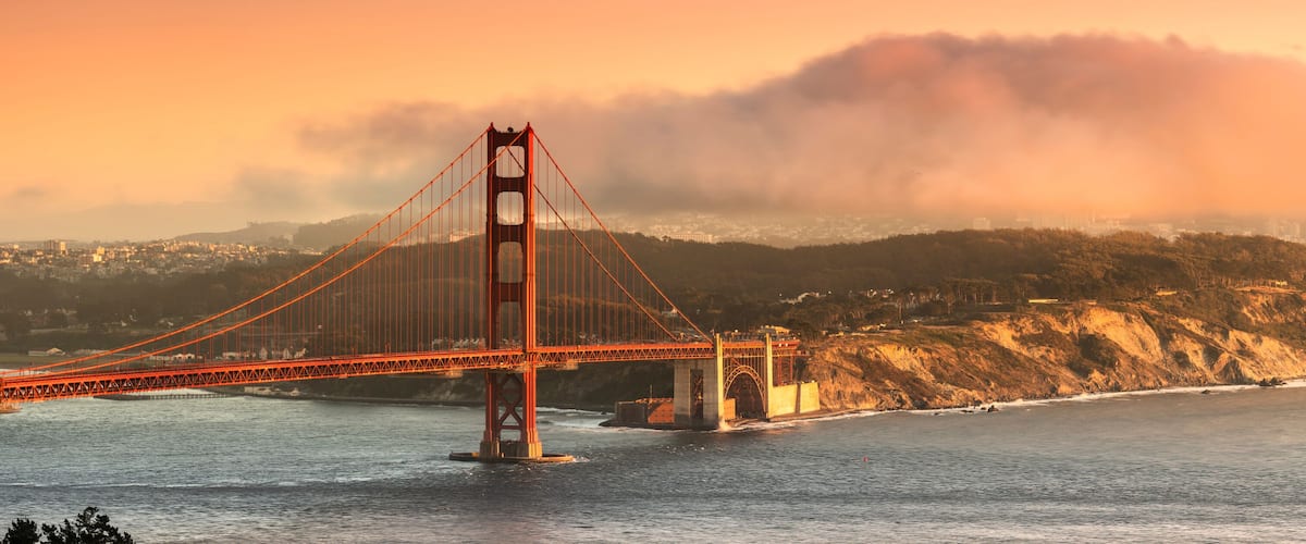 The Golden Gate Bridge with a backdrop of fog and hills.