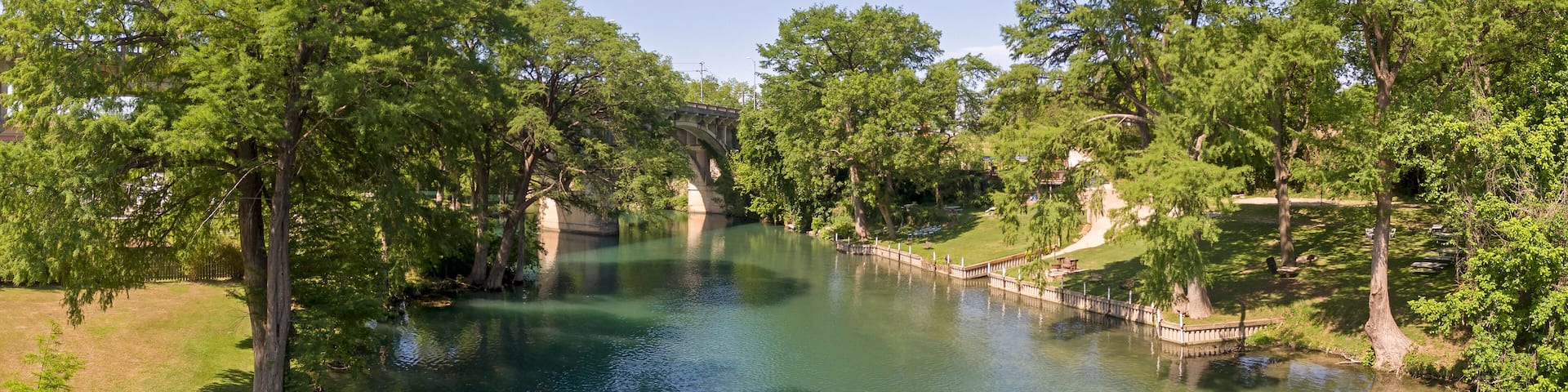 A river with a bridge, surrounded by trees and grassy areas.