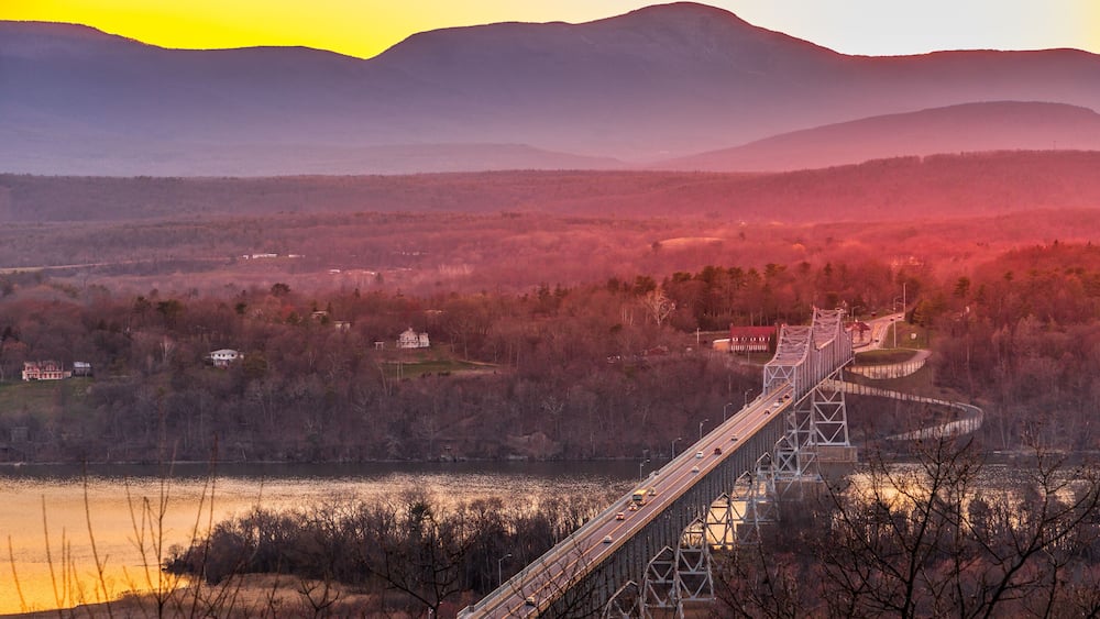 A suspension bridge over a river with mountains in the background.